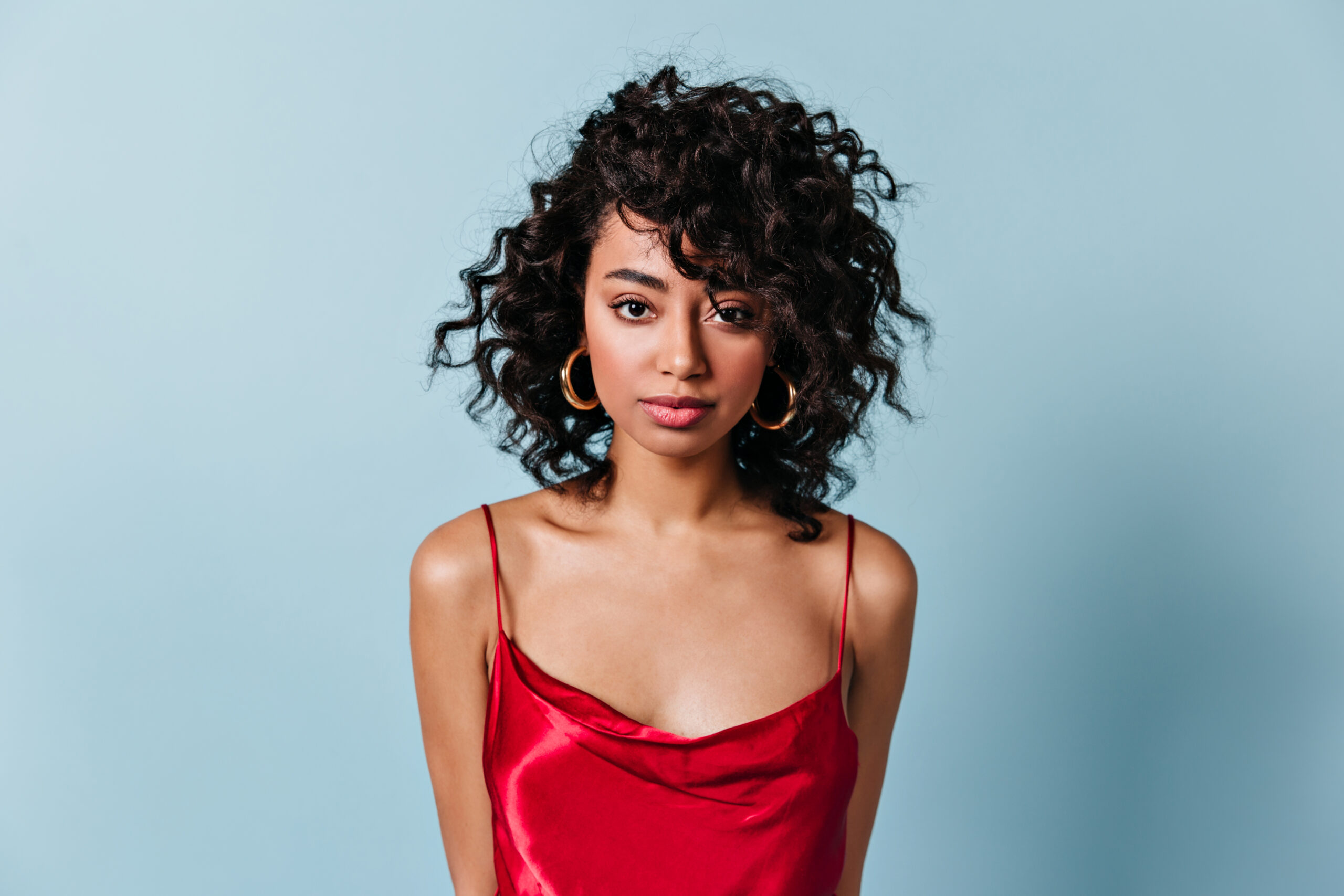 Front view of elegant curly woman. Sensual young lady in red dress looking at camera