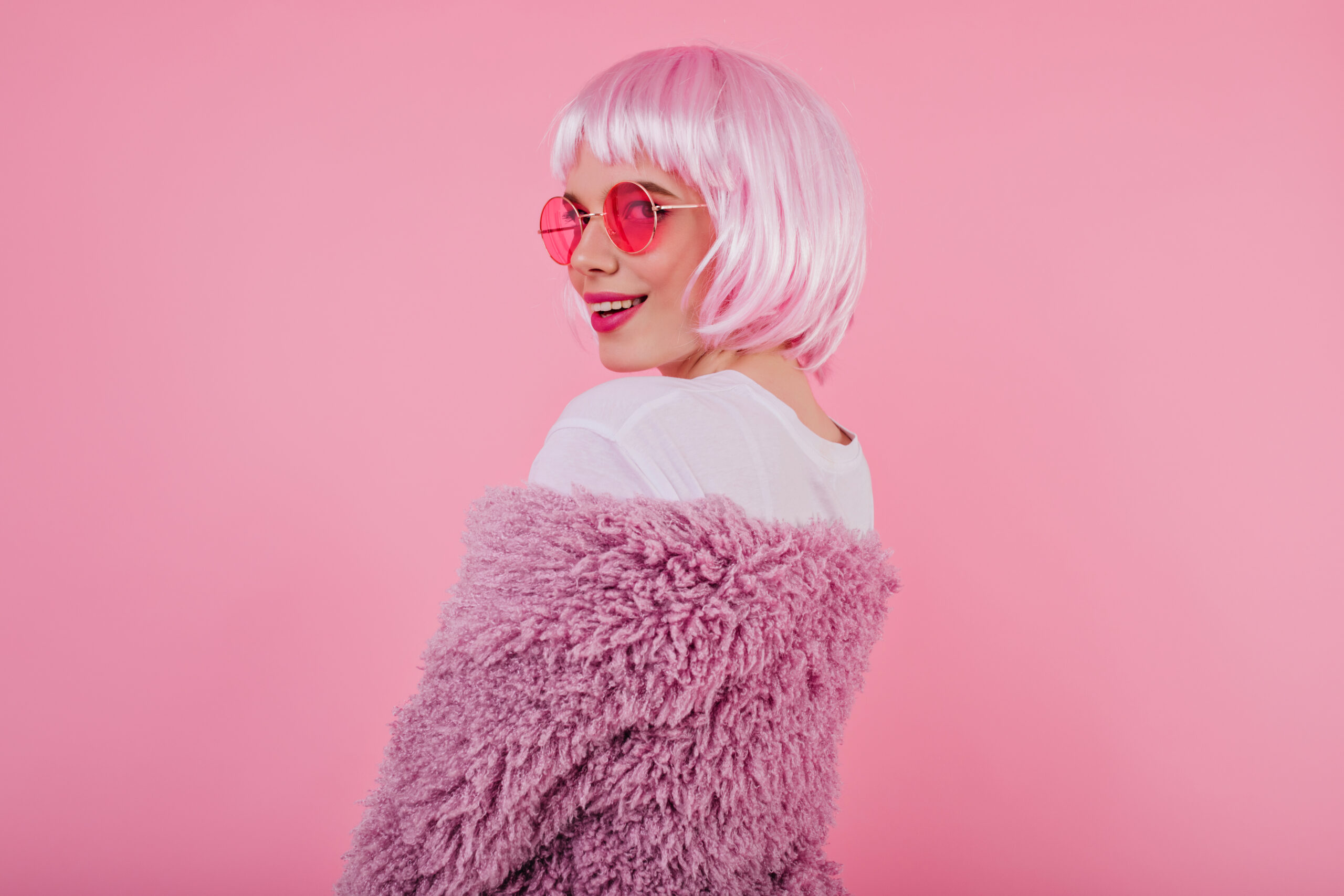 Portrait of playful girl in shiny pink peruke and sunglasses. De